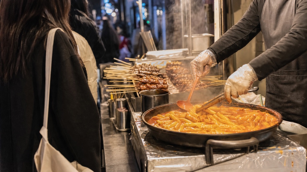 Street food stalls with tteokbokki and skewers in a Hongdae alley at night