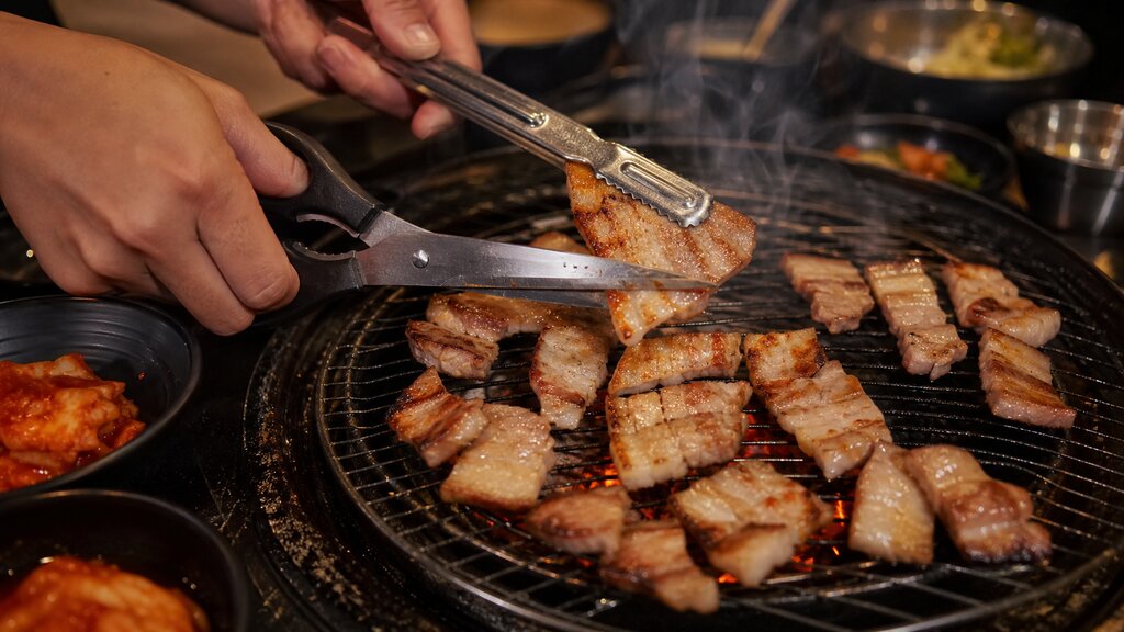 Grilling pork belly with tongs and scissors on a charcoal grill at a Korean BBQ restaurant