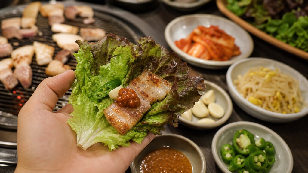 Ssam wrap with grilled pork, lettuce, and assorted banchan side dishes at a Korean BBQ table