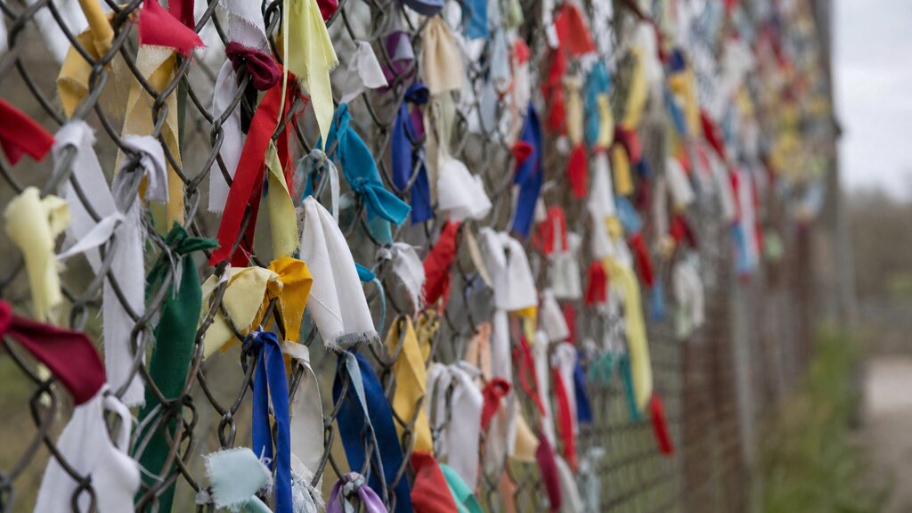 Colorful ribbons and handwritten messages tied to a wire border fence at Imjingak, with small memorial elements below