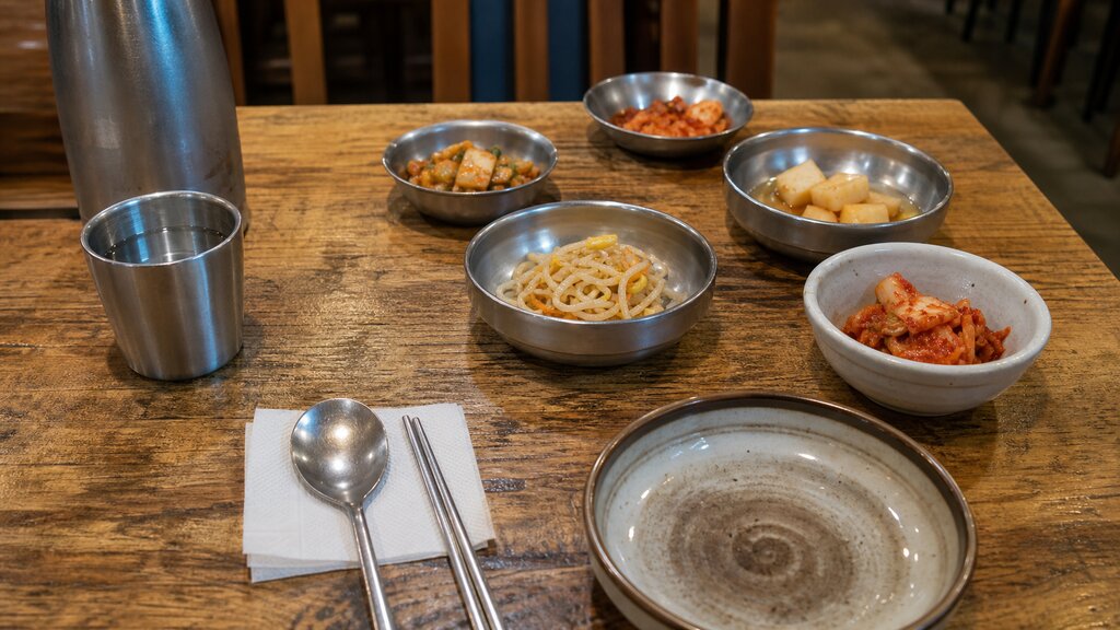 A casual Korean restaurant table set with small banchan side dishes and a self-serve water cup