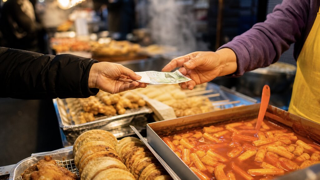 A first-time visitor handing over cash for street food at a busy traditional market stall in Seoul