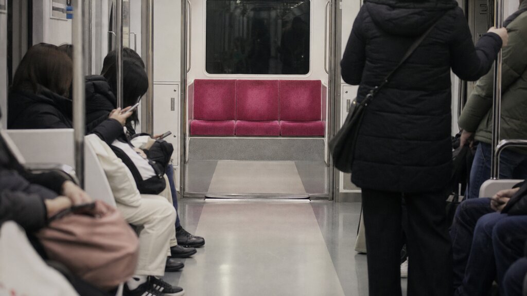 Empty priority seats at the end of a Seoul subway car marked in a different color while other seats are occupied