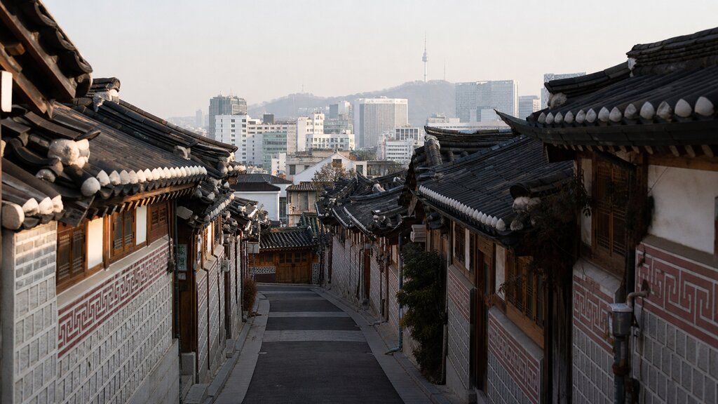 A quiet Bukchon alley lined with tiled hanok rooftops and the modern Seoul skyline rising behind